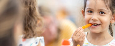 A girl snacking on a carrot stick in school, following a healthy habit.