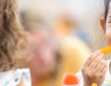 A girl snacking on a carrot stick in school, following a healthy habit.