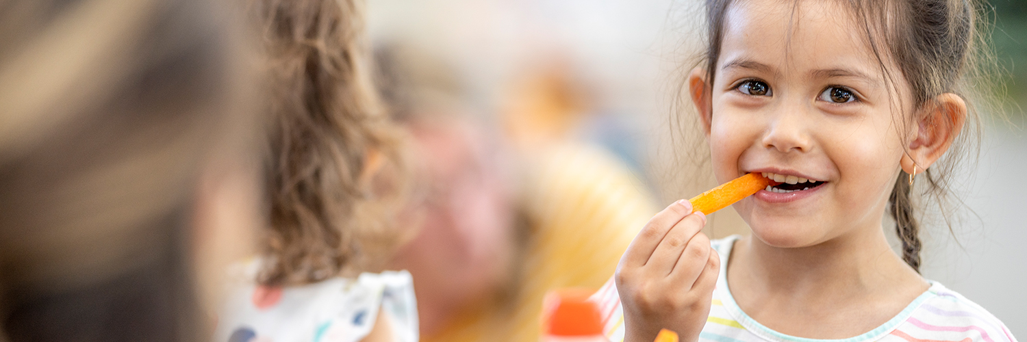 A girl snacking on a carrot stick in school, following a healthy habit.