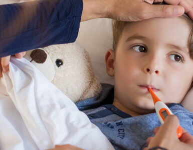 A boy laying in bed, having his temperature taken by his mother to determine if he should go to urgent care of the emergency room.