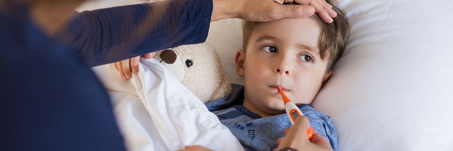 A boy laying in bed, having his temperature taken by his mother to determine if he should go to urgent care of the emergency room.