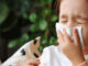 A little girl sitting on the couch, blowing her nose because she has a cold.