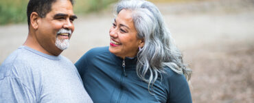 A middle-aged woman sitting on a bench with her husband, smiling at him.