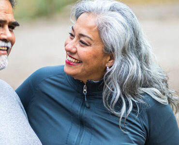 A middle-aged woman sitting on a bench with her husband, smiling at him.
