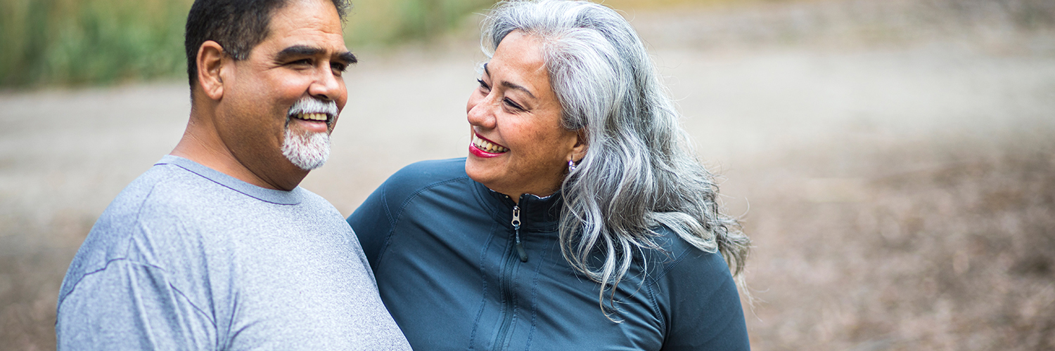 A middle-aged woman sitting on a bench with her husband, smiling at him.