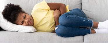 A child curled up on the couch in pain, showing signs of appendicitis.