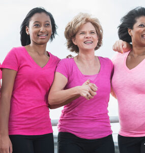 A group of women standing together during a breast cancer awareness walk, wearing pink shirts.