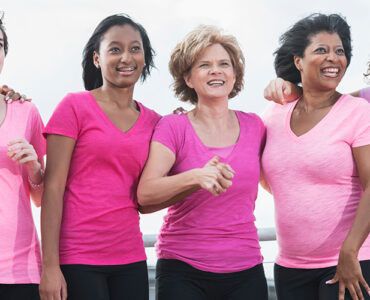 A group of women standing together during a breast cancer awareness walk, wearing pink shirts.