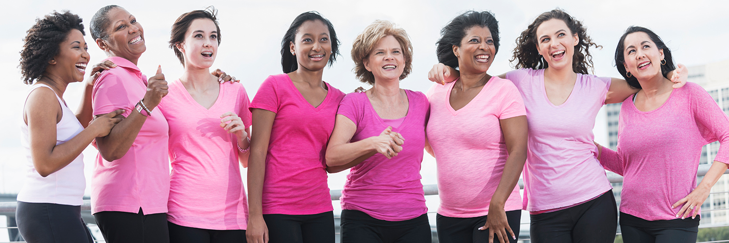 A group of women standing together during a breast cancer awareness walk, wearing pink shirts.