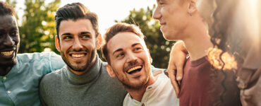 A group of men laughing together outdoors, taking protective measures against mpox in their private lives.