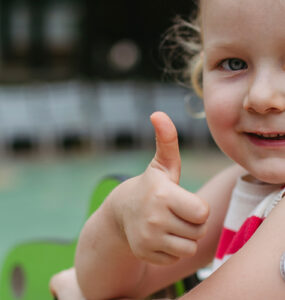 A little girl with childhood diabetes giving a thumbs up while at playing at the park.