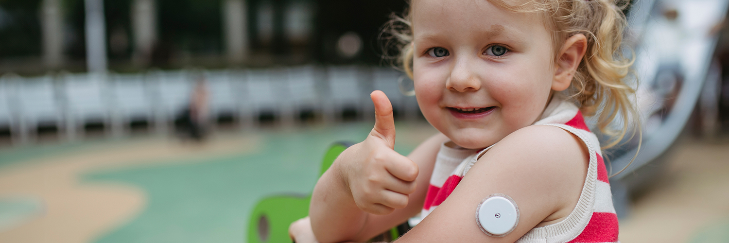 A little girl with childhood diabetes giving a thumbs up while at playing at the park.