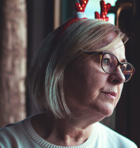 A woman looking out the window, grieving the loss of her loved one during the holiday season.