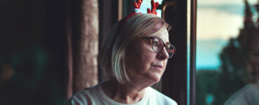 A woman looking out the window, grieving the loss of her loved one during the holiday season.