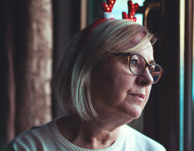 A woman looking out the window, grieving the loss of her loved one during the holiday season.