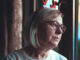 A woman looking out the window, grieving the loss of her loved one during the holiday season.