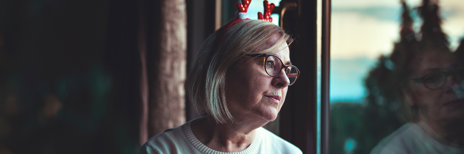 A woman looking out the window, grieving the loss of her loved one during the holiday season.