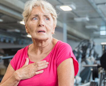 A woman with her hand over her chest while at the gym exercising, experiencing heart palpitations due to AFib.