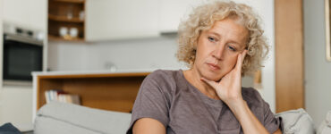 A woman looking melancholy on the coach, dealing with early signs of Huntington's Disease.