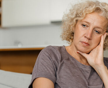A woman looking melancholy on the coach, dealing with early signs of Huntington's Disease.
