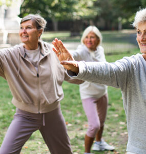 A group of women in a park doing tai chi together as part of their beginner exercise routine.