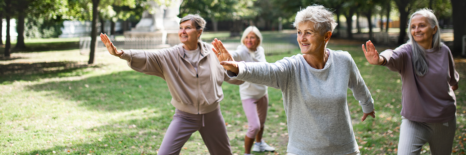 A group of women in a park doing tai chi together as part of their beginner exercise routine.