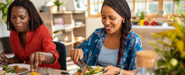 Two women sitting at the table together, eating healthy whole and plant-based foods.