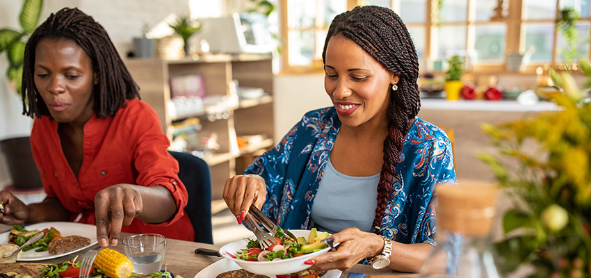 Two women sitting at the table together, eating healthy whole and plant-based foods.