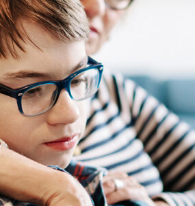 A boy sits with his mother on their living room couch, looking over online resources about transgender youth support.