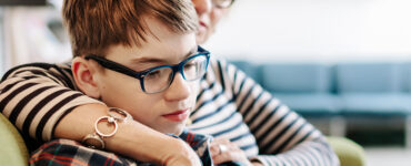 A boy sits with his mother on their living room couch, looking over online resources about transgender youth support.