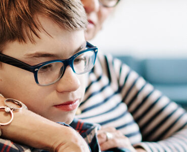 A boy sits with his mother on their living room couch, looking over online resources about transgender youth support.