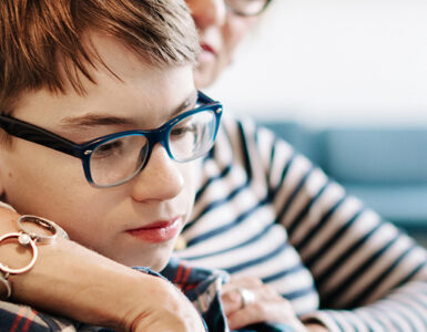 A boy sits with his mother on their living room couch, looking over online resources about transgender youth support.