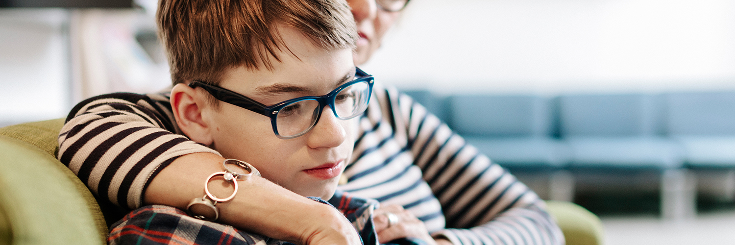 A boy sits with his mother on their living room couch, looking over online resources about transgender youth support.