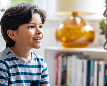A boy sitting down and looking at his mother, who is noticing his involuntary movements, or tics.