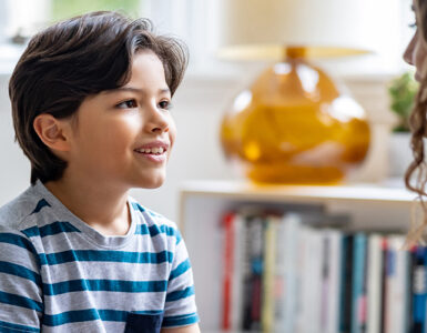 A boy sitting down and looking at his mother, who is noticing his involuntary movements, or tics.