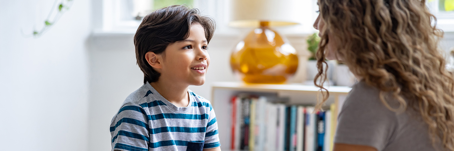 A boy sitting down and looking at his mother, who is noticing his involuntary movements, or tics.