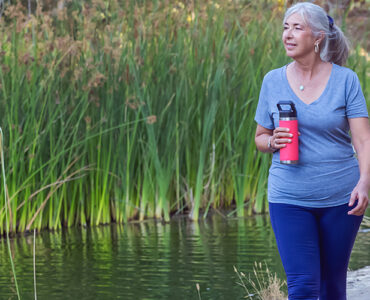 A woman walking outdoors, holding a bottle of water and enjoying her surroundings.