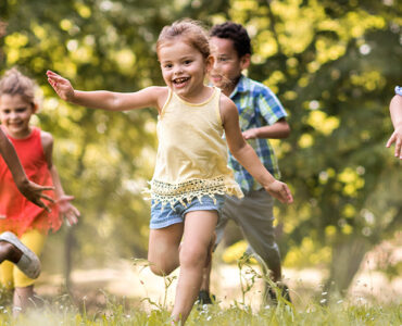 A group of young children running through a field of tall grasses during the summertime.