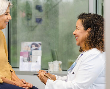 An older woman sitting with a female physician in an examination room, having a heart exam.