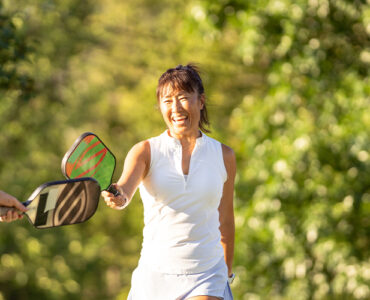 A middle-aged man and woman playing pickle ball outdoors, smiling.