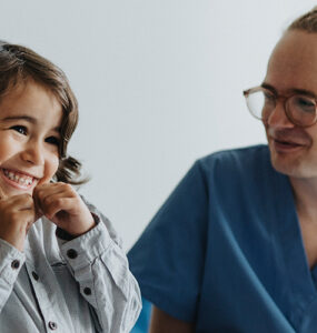 A young boy sitting next to his mother, smiling at his developmental and behavioral pediatricians.