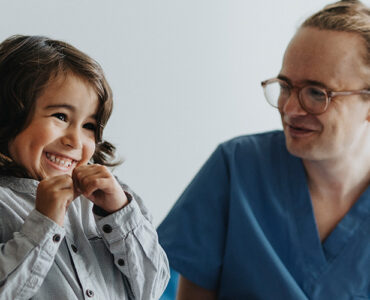 A young boy sitting next to his mother, smiling at his developmental and behavioral pediatricians.