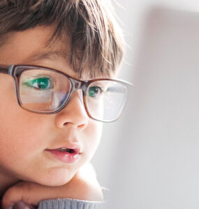A young boy wearing glasses, looking into a laptop computer.