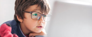 A young boy wearing glasses, looking into a laptop computer.