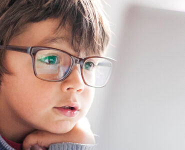 A young boy wearing glasses, looking into a laptop computer.