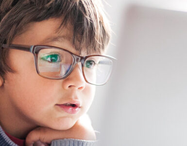 A young boy wearing glasses, looking into a laptop computer.