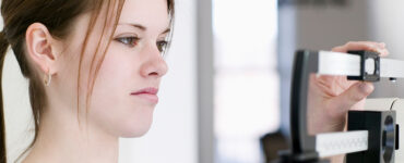 A teenage girl weighing herself on a scale, looking at the results with a frown on her face.