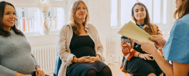 A group of pregnant women sitting in a circle, receiving group support from their midwife.