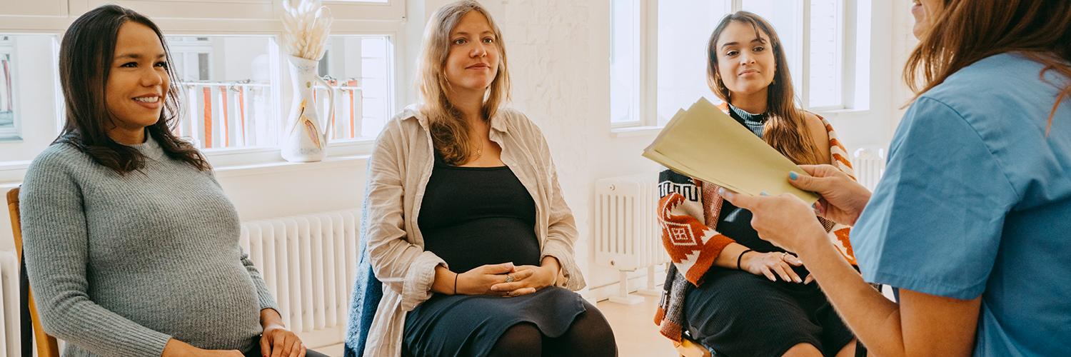 A group of pregnant women sitting in a circle, receiving group support from their midwife.