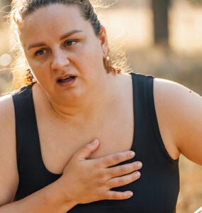 A woman walking outdoors, looking like she's in pain and out of breath.